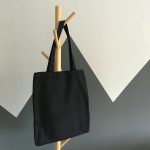 Simple and elegant black canvas tote bag hanging on a wooden rack, perfect for eco-friendly shopping.