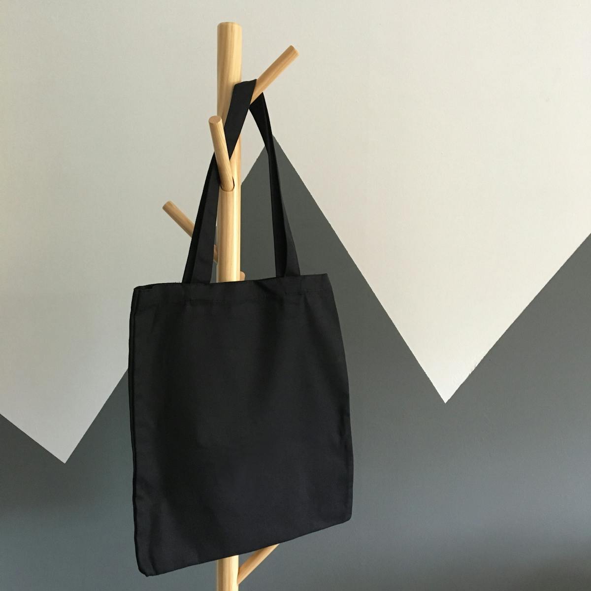 Simple and elegant black canvas tote bag hanging on a wooden rack, perfect for eco-friendly shopping.