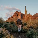 A hiker climbs a desert trail towards mountains.