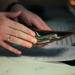 Hands holding cash in a wallet over papers
