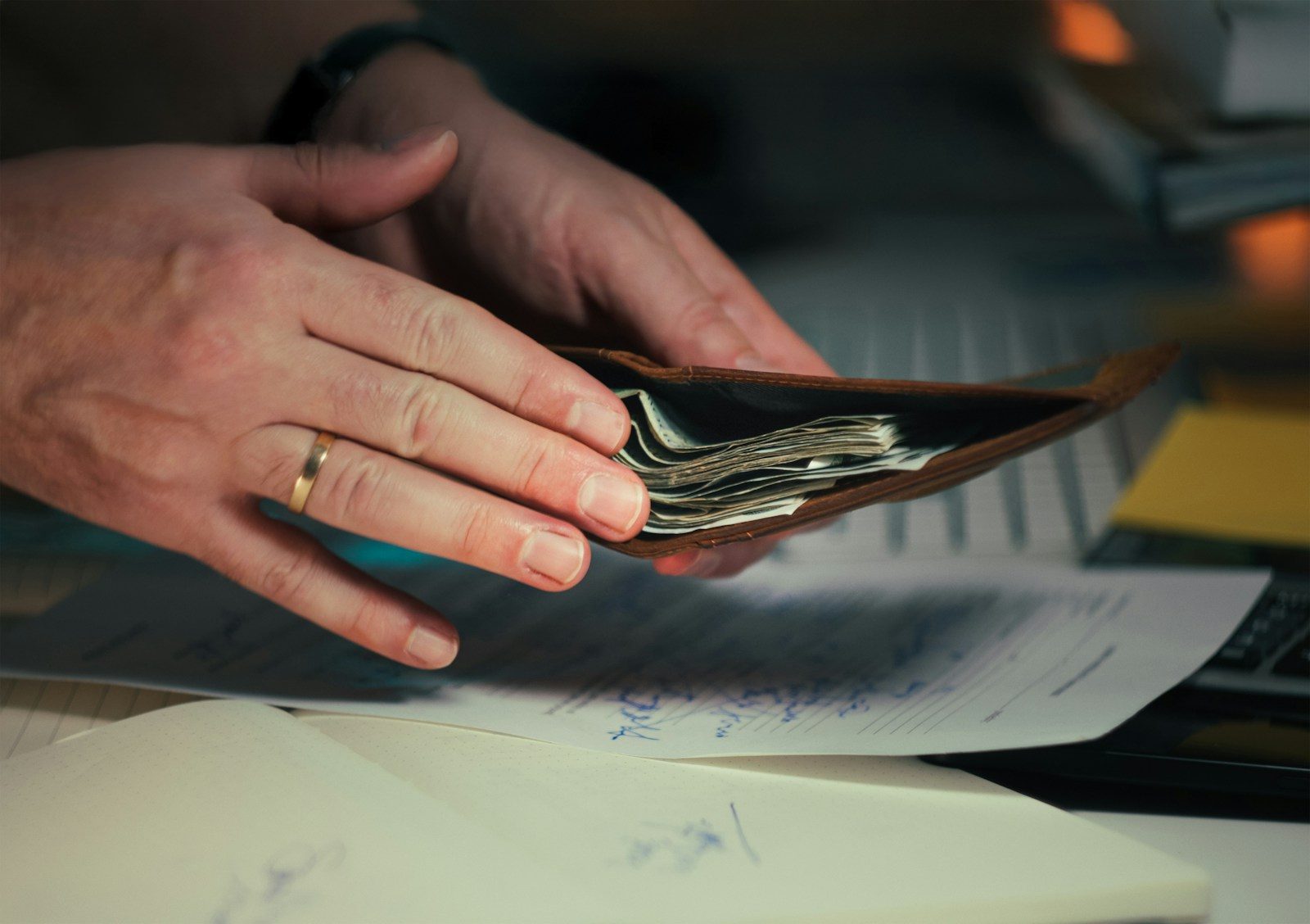 Hands holding cash in a wallet over papers